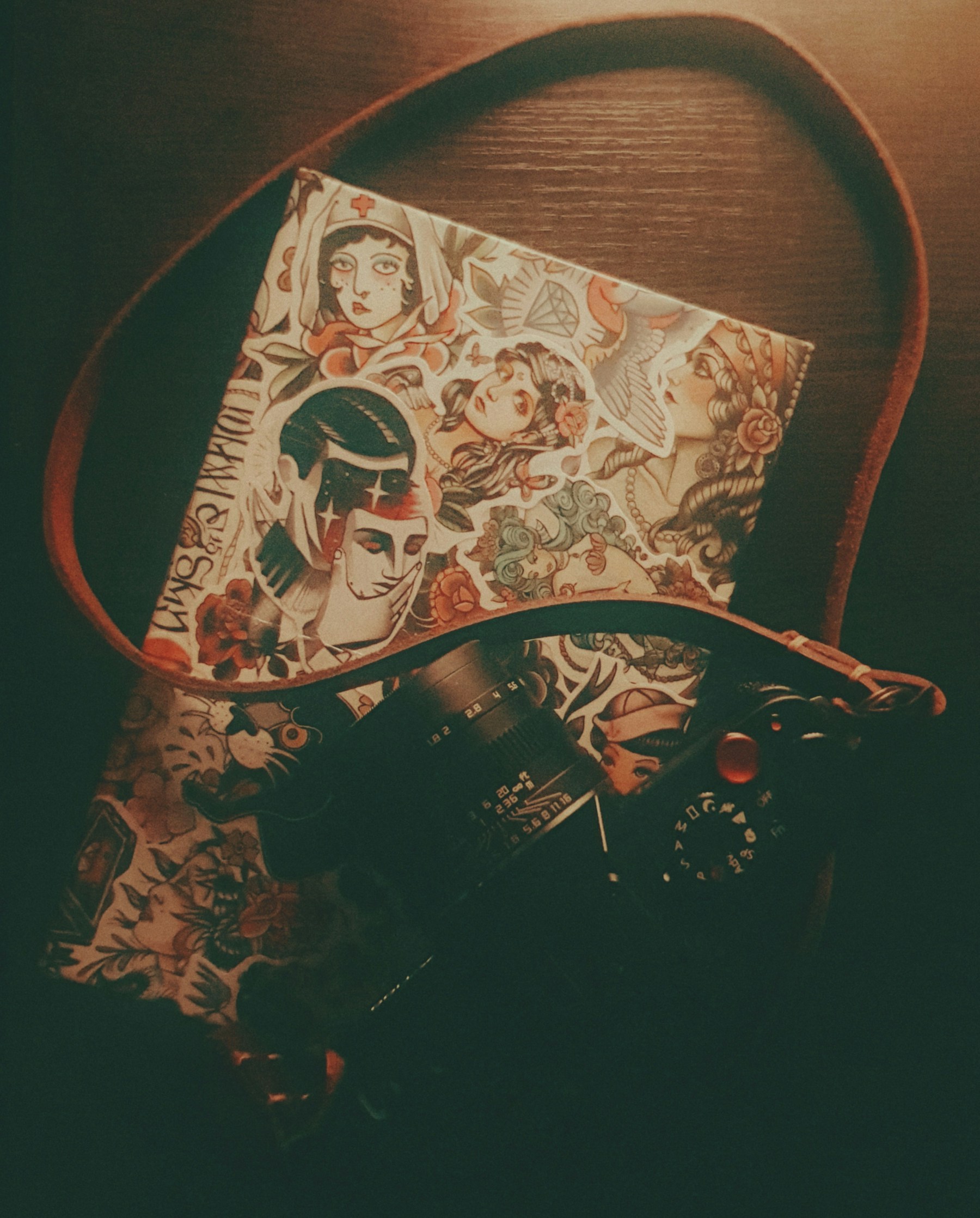A camera and a notebook decorated with tattoo-style artwork on a wooden surface